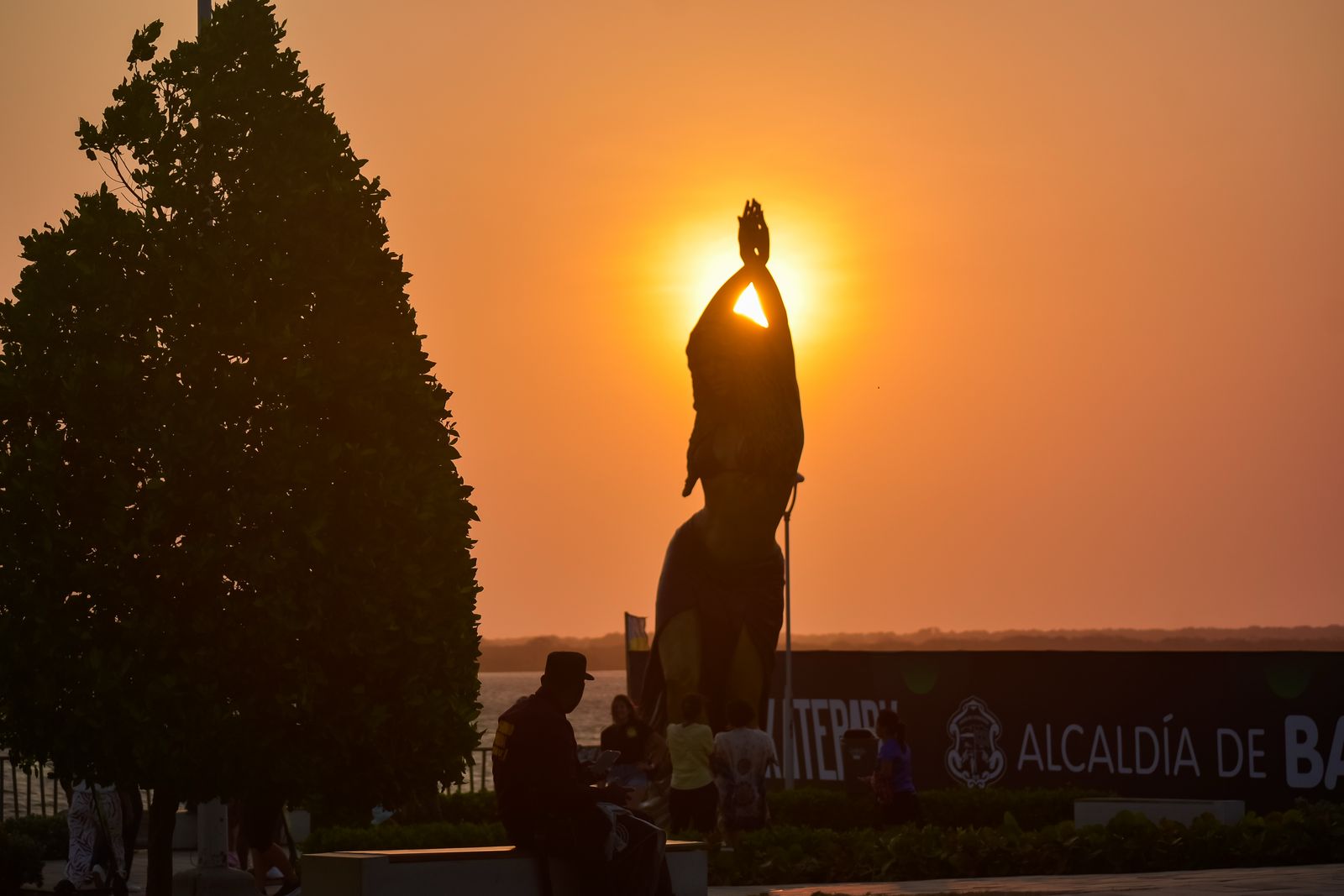 Vista de estatua de Shakira en el Gran Malecón de Barranquilla al atardecer, con cielo cálido y ambiente tranquilo.