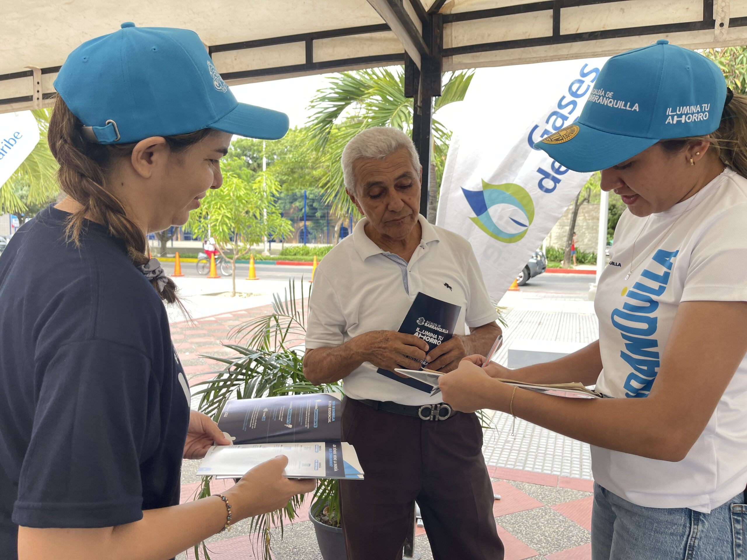 Funcionarias de la Alcaldía de Barranquilla socializan con ciudadano la campaña “Ilumina tu Ahorro” mediante folleto informativo.