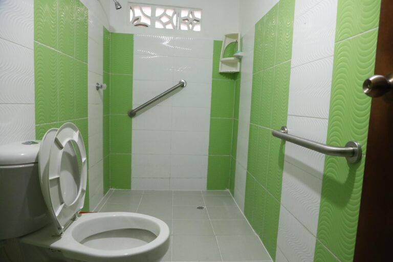 Baño remodelado con paredes de cerámica verde y blanca, equipado con barras de apoyo para accesibilidad y mayor seguridad.