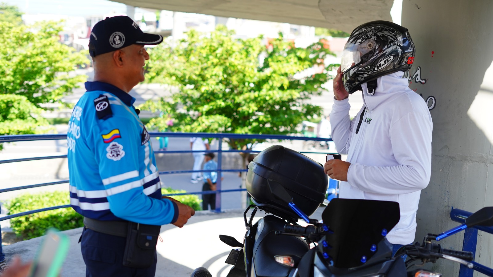 Agente de tránsito de Barranquilla realiza labor pedagógica con motociclista en puente peatonal.