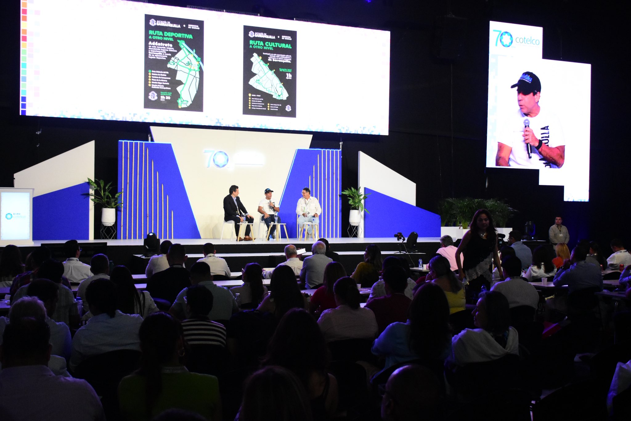 Evento institucional con público asistente; en tarima, el alcalde Char participa como ponente junto a dos panelistas.
