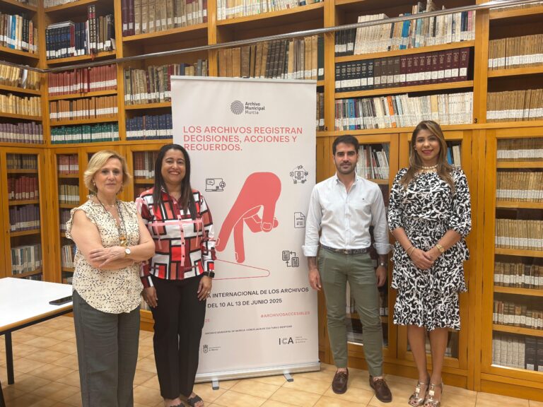Grupo de personas de pie frente a un banner, sonriendo y posando para la foto en el Archivo Municipal de Murcia.