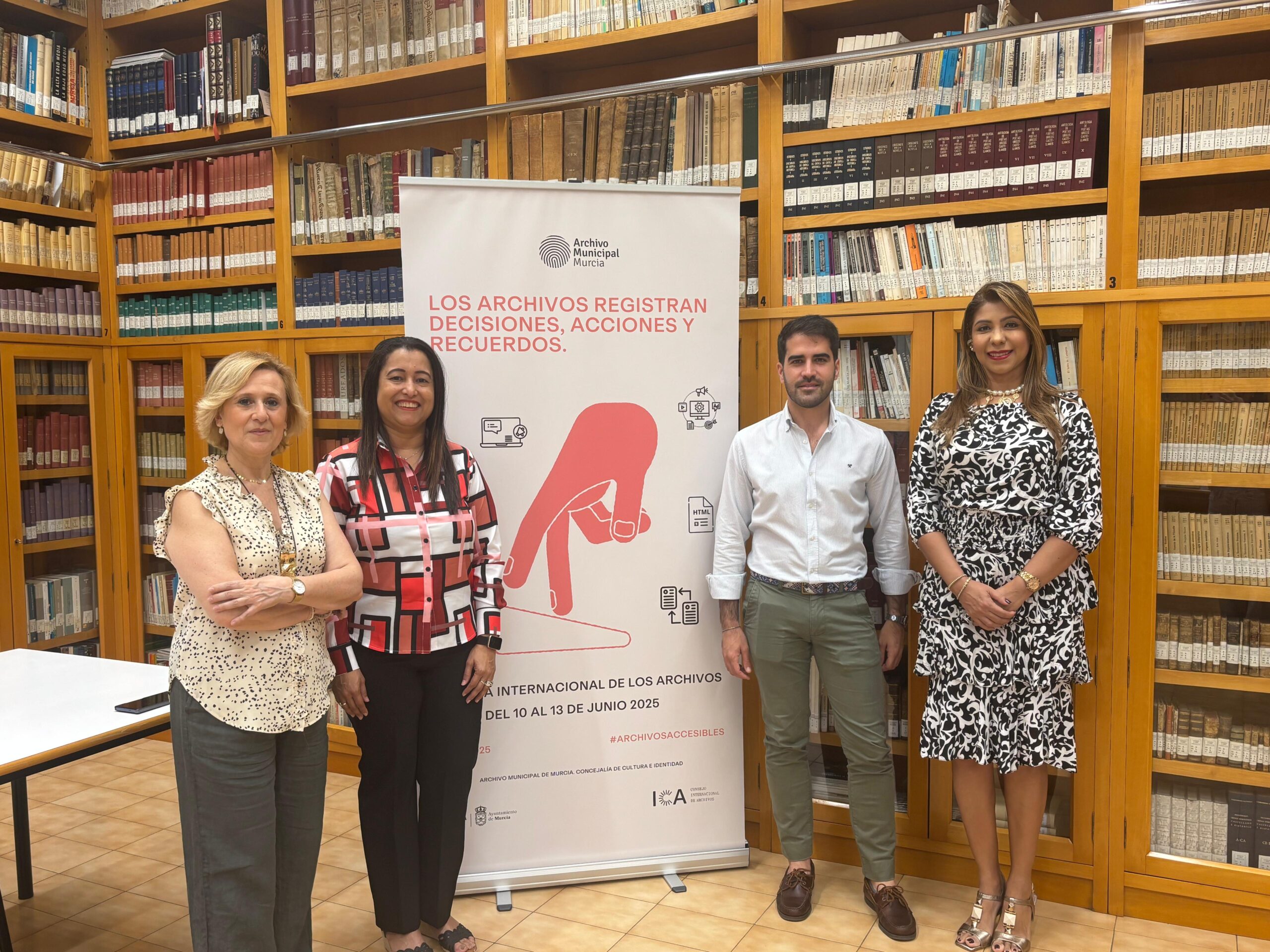 Grupo de personas de pie frente a un banner, sonriendo y posando para la foto en el Archivo Municipal de Murcia.