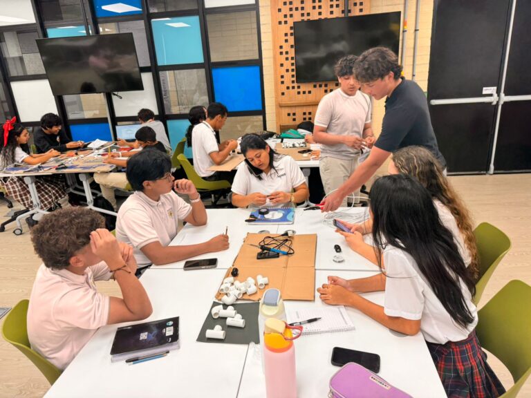 Estudiantes sentados en un aula trabajan en equipo en actividades tecnológicas del programa BAQSTEM+IS Sin Fronteras.