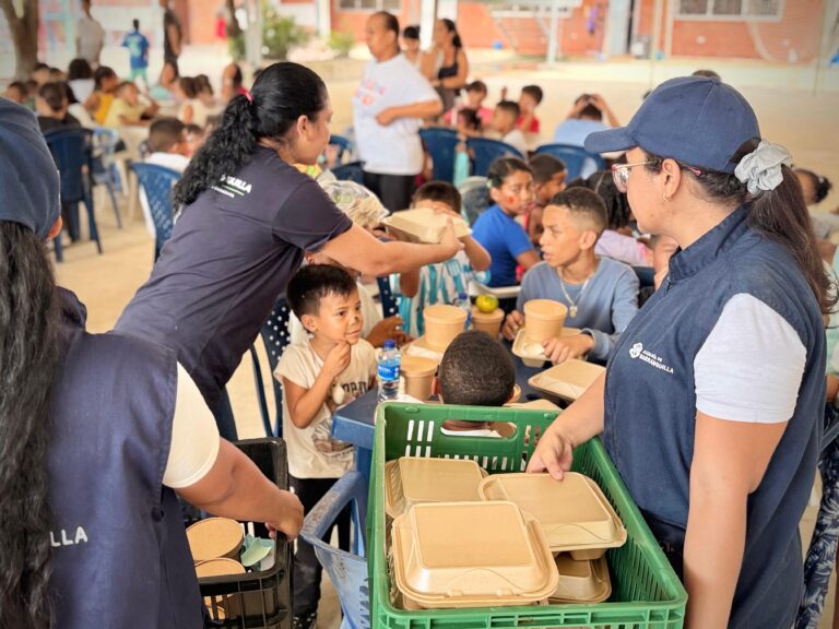 En la imagen, varios niños y niñas del barrio La Paz están sentados en mesas al aire libre mientras reciben alimentos de parte de servidores públicos. Esta actividad hace parte del programa de Comedores Comunitarios, impulsado por el alcalde Alejandro Char, que cada sábado beneficia a más de 200 menores con alimentación saludable y espacios recreativos.