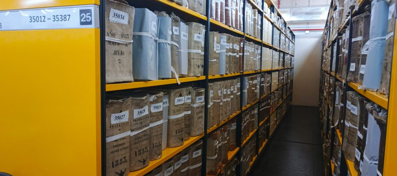 Imagen de un pasillo con estantes de archivos foliados.