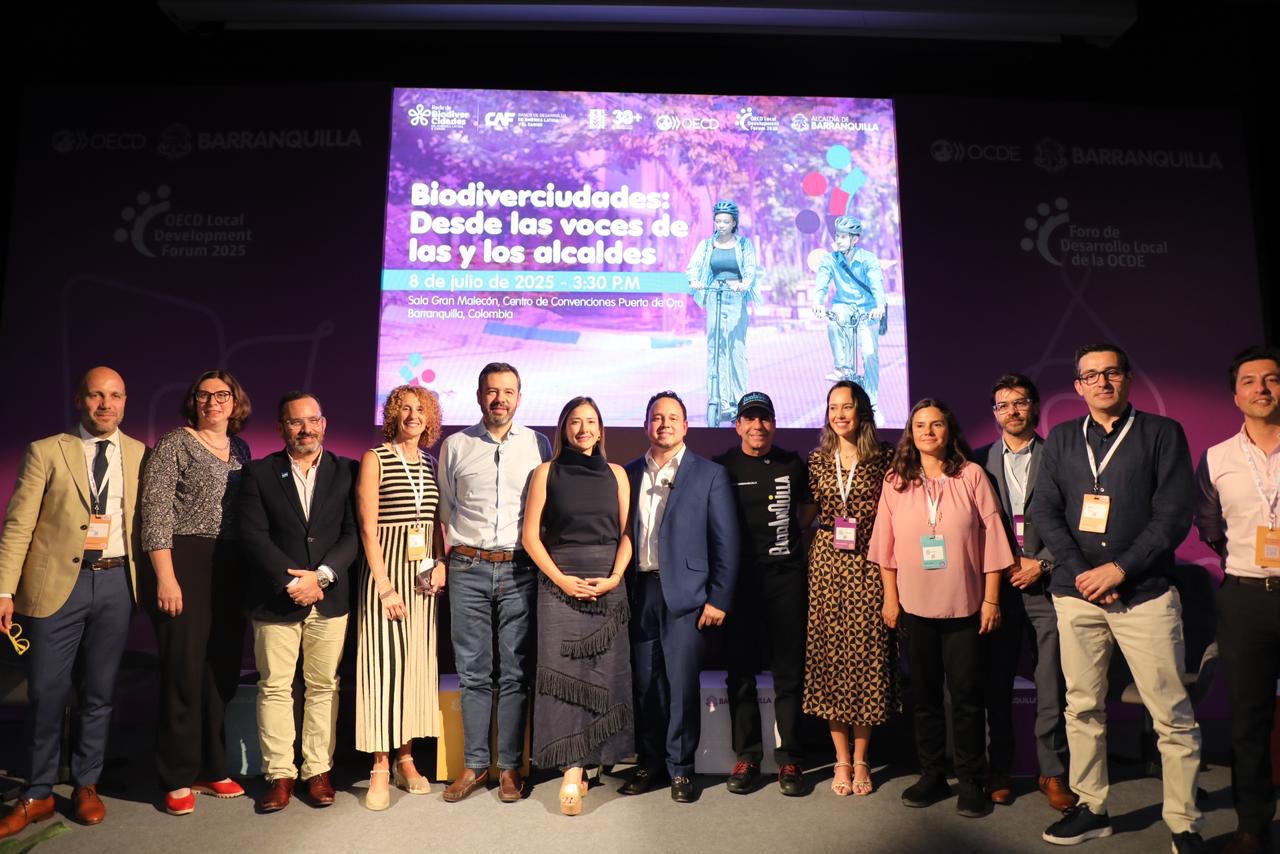 Grupo de expertos y autoridades posa frente a pantalla que anuncia “Biodiverciudades: desde las voces de los y las alcaldes”, en en evento OCDE 2025.