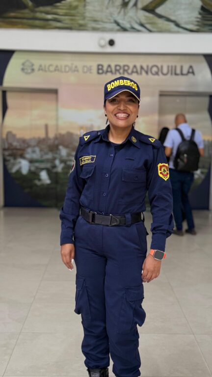 Diana Balza, sonriente de pie en el edificio de la Alcaldía de Barraquilla con uniforme de bombera , azul oscuro.