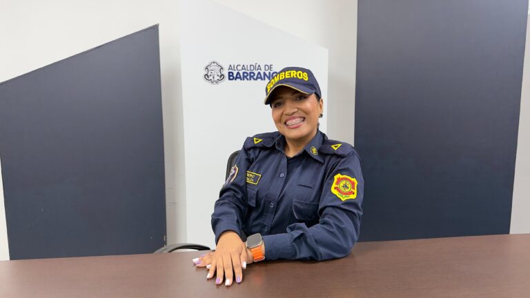Diana Balza sonriente con uniforme de bombera, sentada frente a un fondo de la Alcaldía de Barranquilla.
