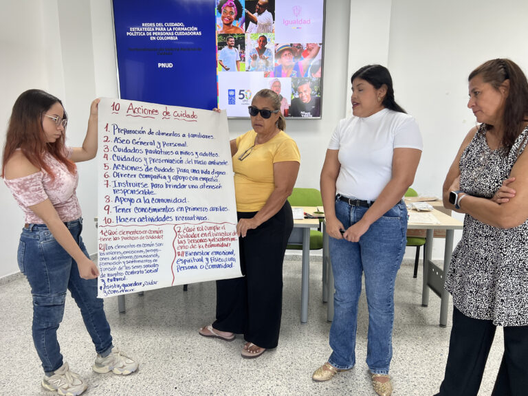 Cuatro mujeres socializan cartel con las “10 Acciones de Cuidado” durante jornada sobre la Economía del Cuidado en Barranquilla.