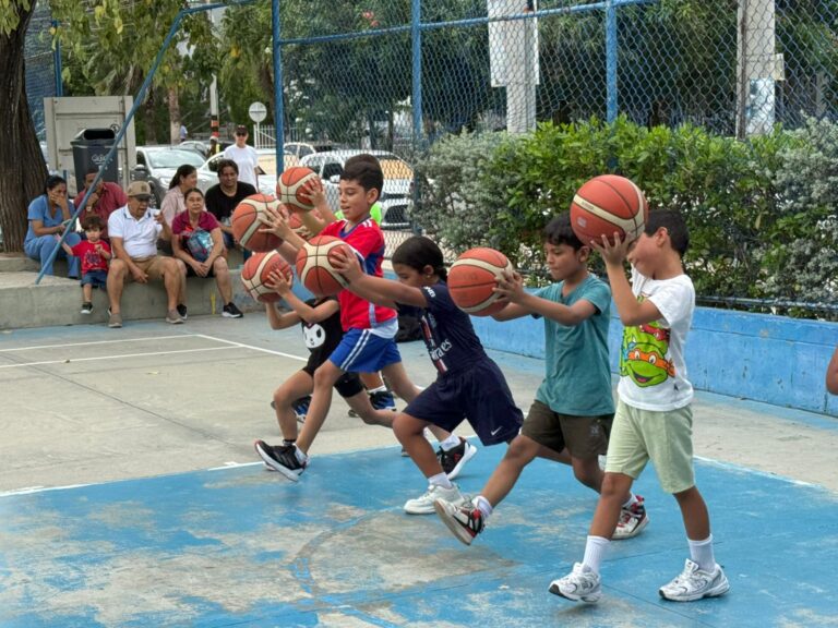 Niños practican técnicas de baloncesto en una clase de formación deportiva al aire libre, observados por familiares.