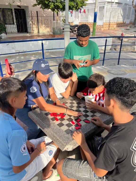 Funcionaria de la alcaldía de Barranquilla acompañada de jóvenes jugando ajedrez en la mesa del parque de Conidec.