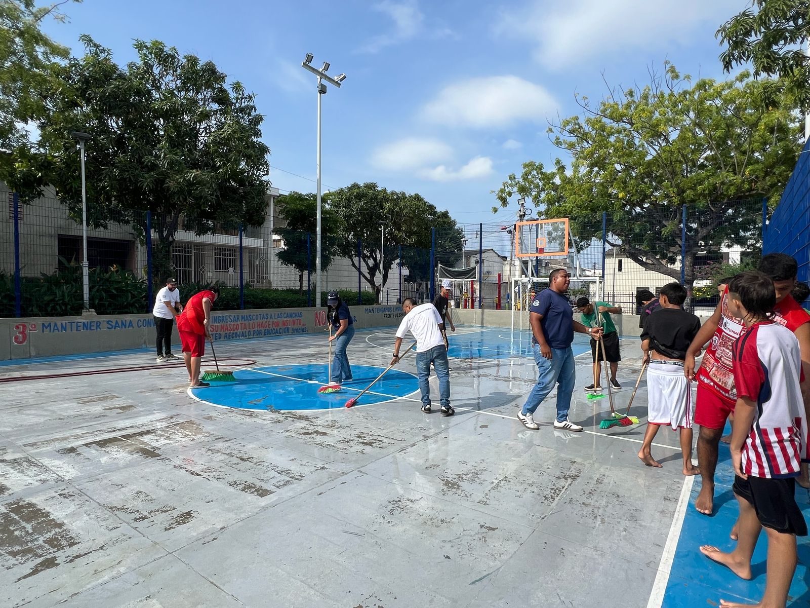 Personas limpian una cancha deportiva mojada con escobas en el parque Conidec.