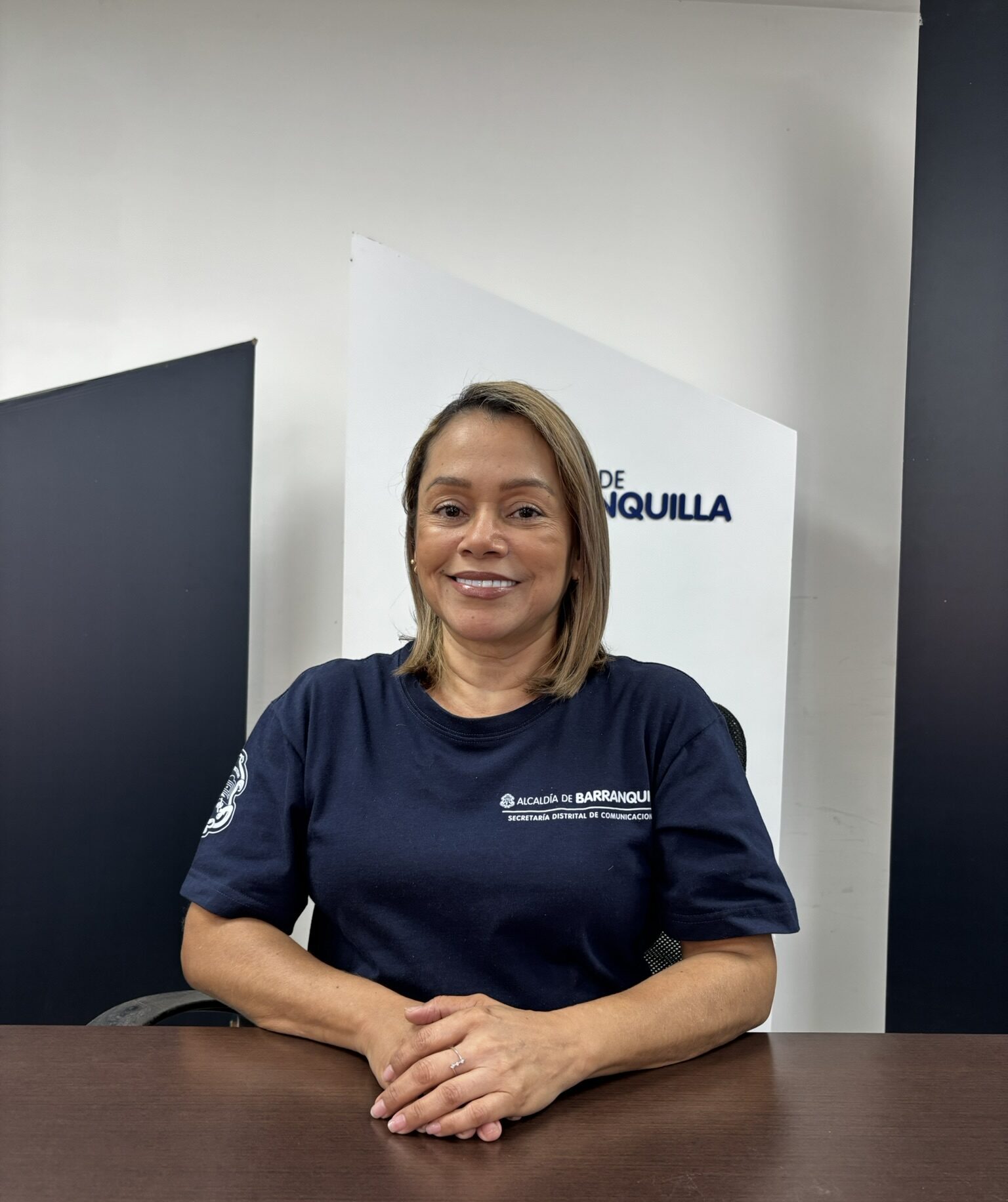 Funcionaria con uniforme institucional, sentada de frente a una mesa, en plano medio.