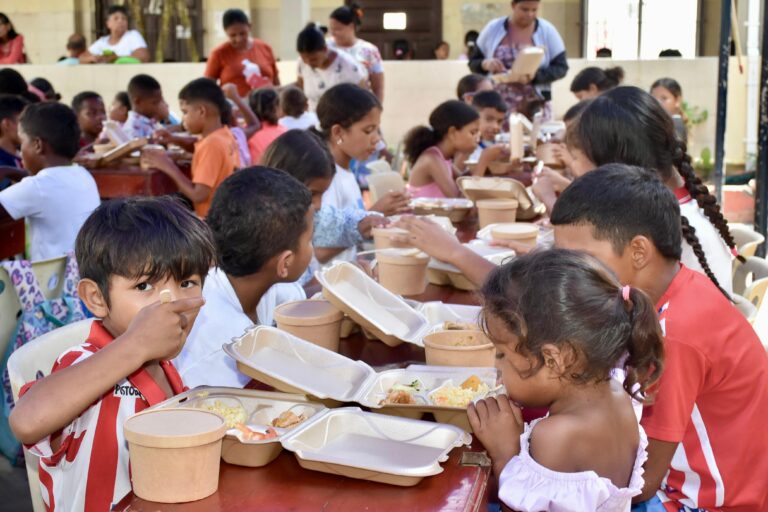 Niños y niñas disfrutan su almuerzo en comedor comunitario con envases biodegradables.