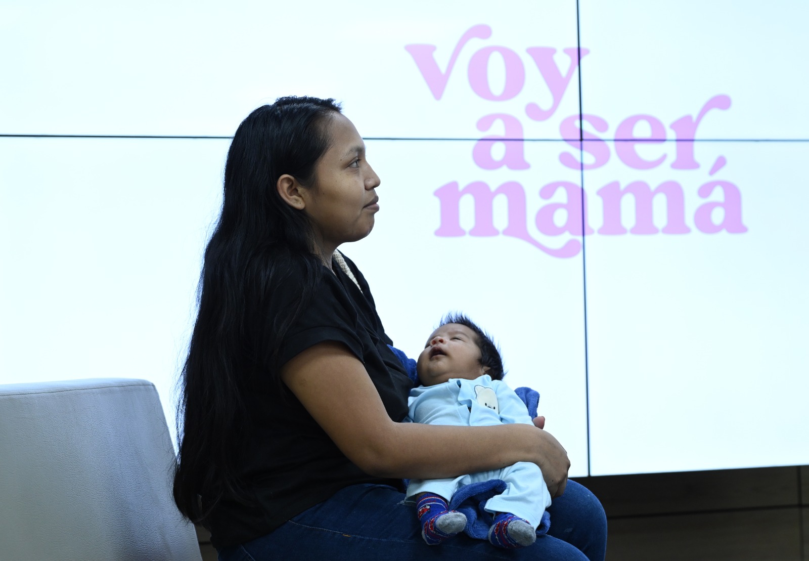 Mujer con su bebé sentada frente a pantalla del programa Voy a Ser Mamá