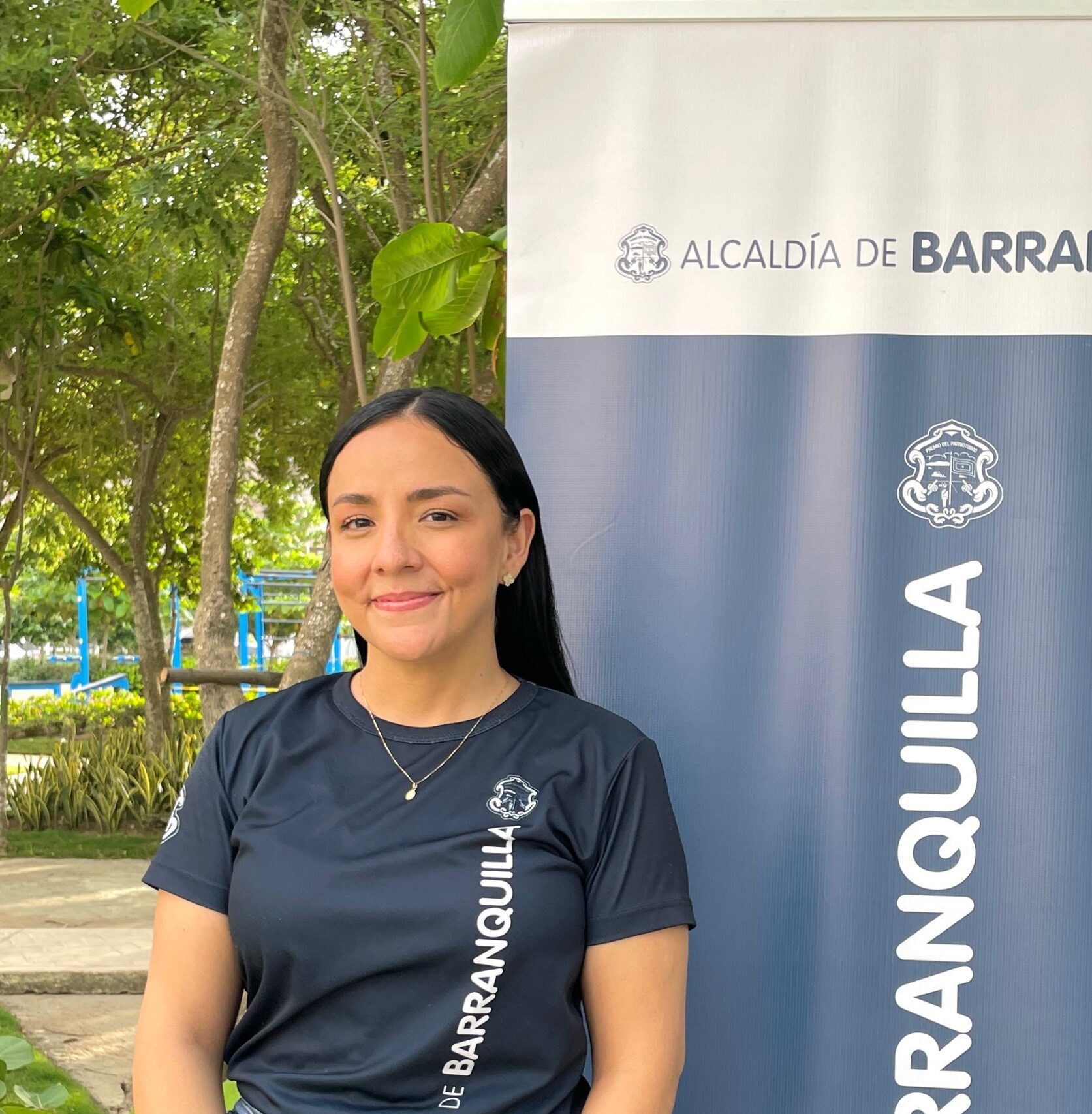 Sugey Correa en plano medio, posa de pie junto a un pendon institucional.