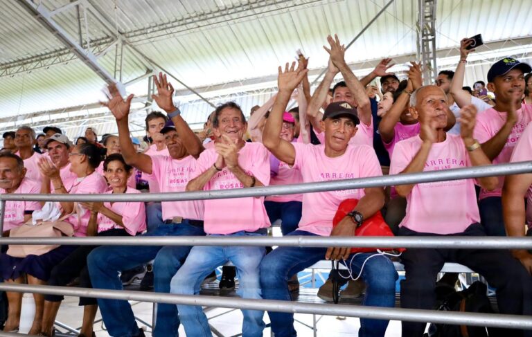 Grupo de adultos mayores con camisetas rosadas participa con entusiasmo en las graderías de un evento.