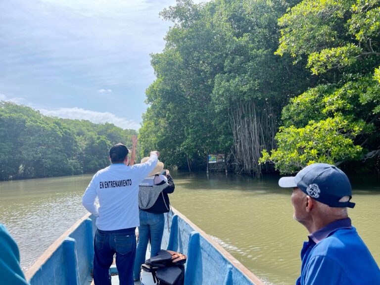 Instructor en bote junto a pescadores recorriendo un canal rodeado de manglares.