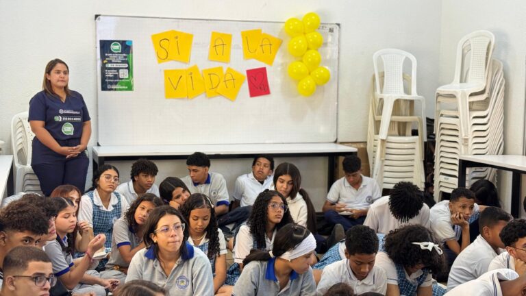 Funcionaria de la Secretaría de Salud con niños en salón de clases junto a un tablero con el letrero: Sí a la Vida en letras amarillas