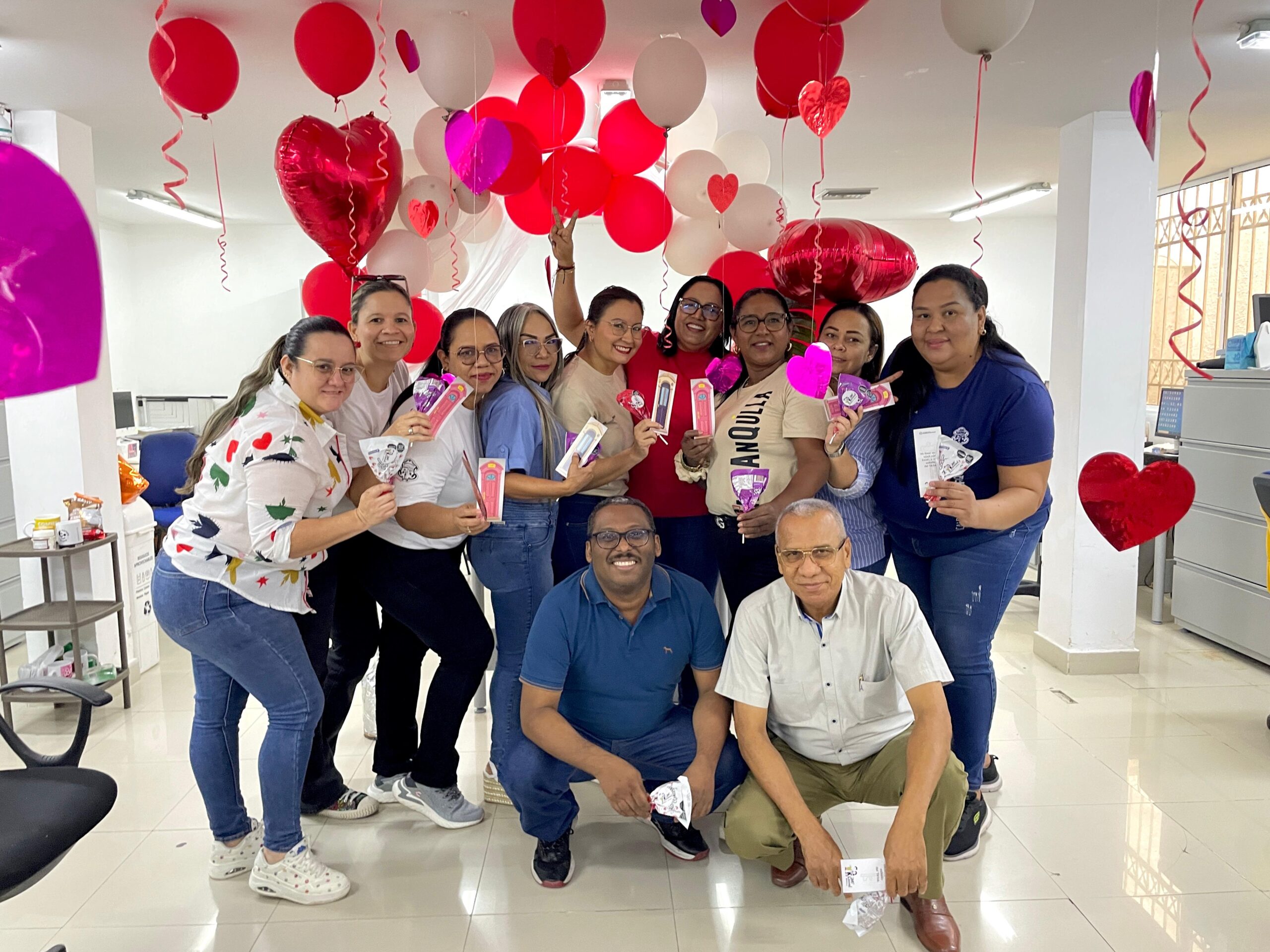Funcionarios en plano abierto general, posan con chupetas de corazones y decoración de amor y amistad.