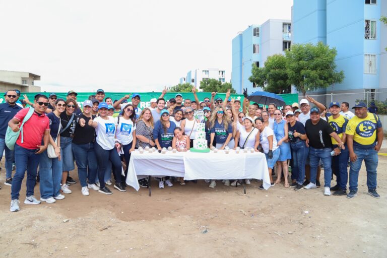 Un grupo de personas sonrientes posa para la cámara frente a una mesa con pastel y vasos.