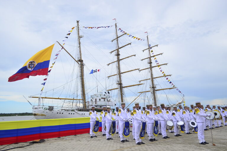 Cadetes de la Armada Nacional formados en puerto junto al buque insignia Gloria, con banderas de Colombia ondeando.