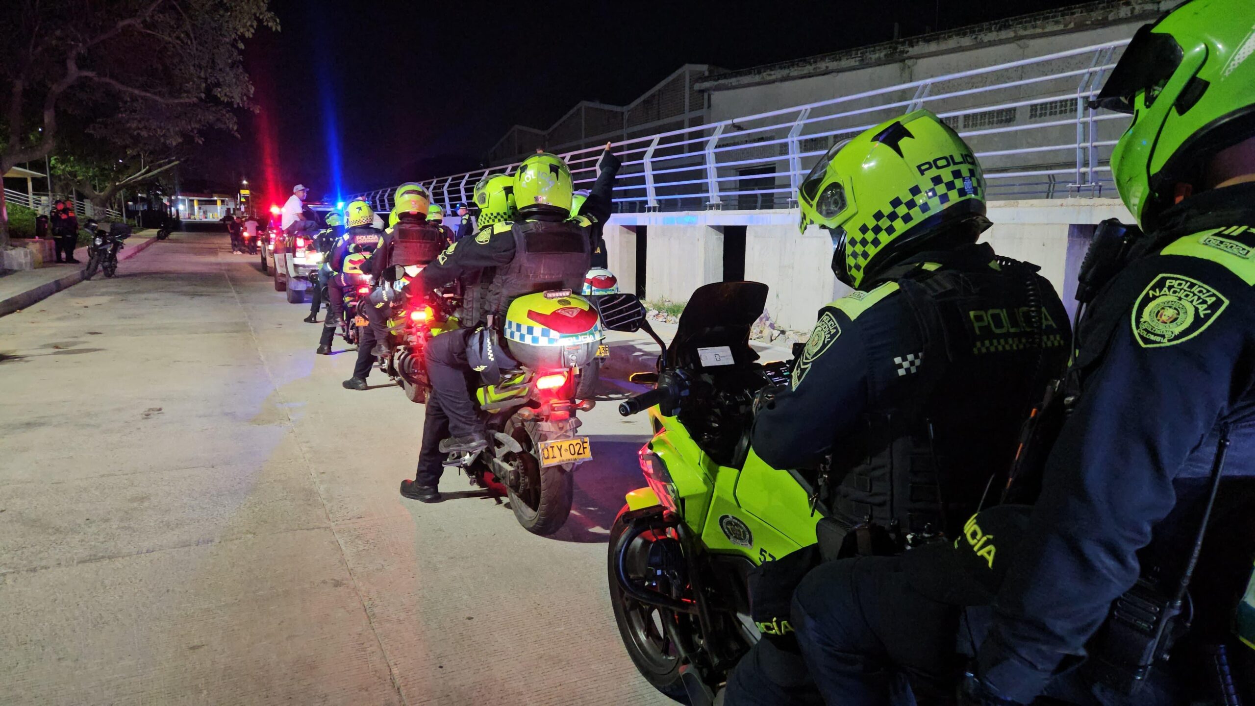 Patrullaje nocturno de la Policía Nacional con unidades motorizadas, luces encendidas y en formación sobre una vía urbana.