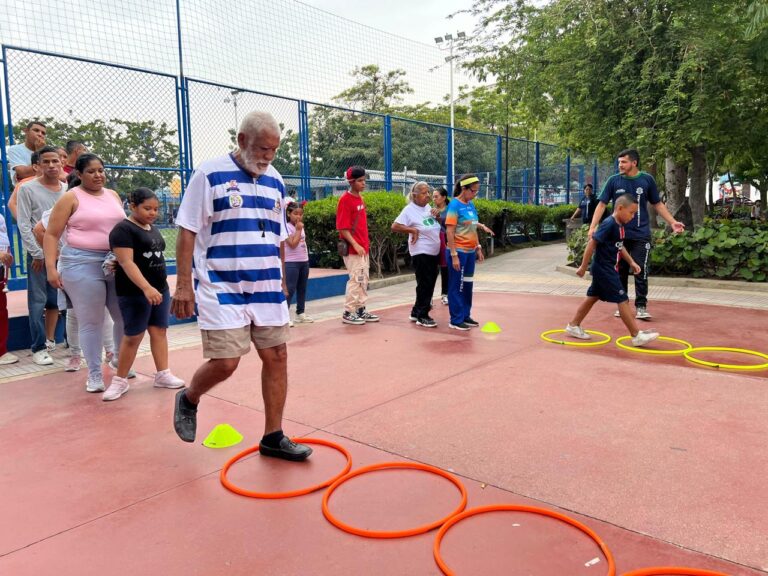 Grupo de personas participan jornadas recreodeportivas en un parque, realizando actividades físicas con aros de colores en el suelo.