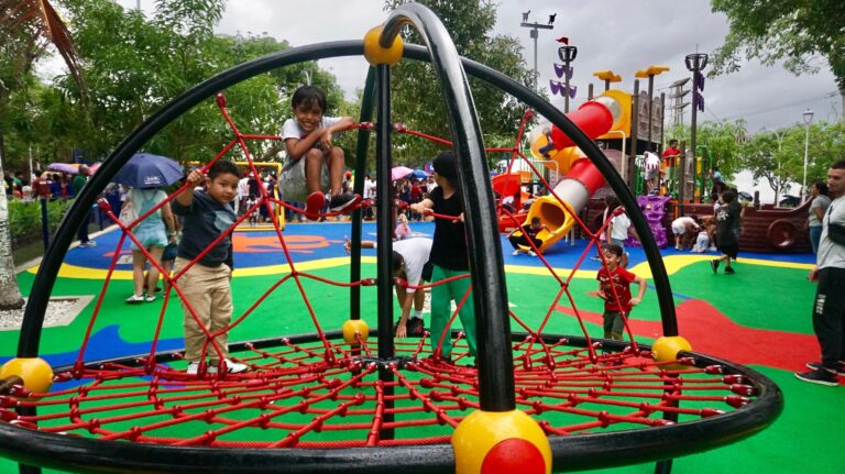 Niños jugando en el parque La Solución, con estructuras de cuerdas, toboganes y algunos adultos presentes.
