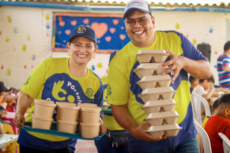 Dos enlaces de cultura ciudadana en el comedor comunitario de barrio Gálan con cajas de almuerzos en las manos.