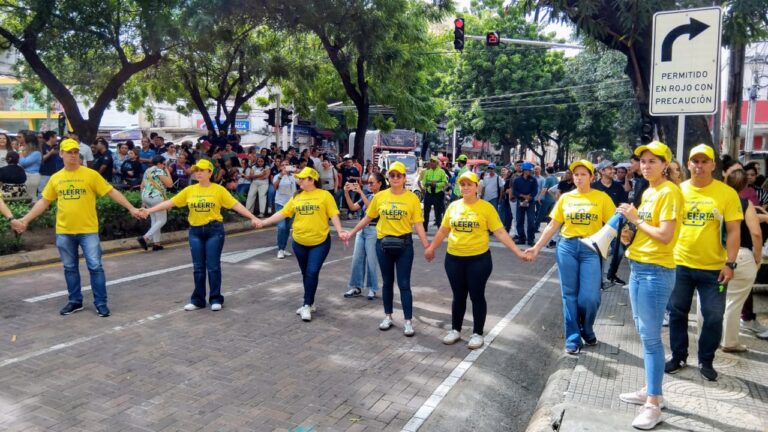 Fila de funcionarios con camiseta y gorra amarilla promoviendo el logo del simulacro en la calle 34, frente a la Alcaldía