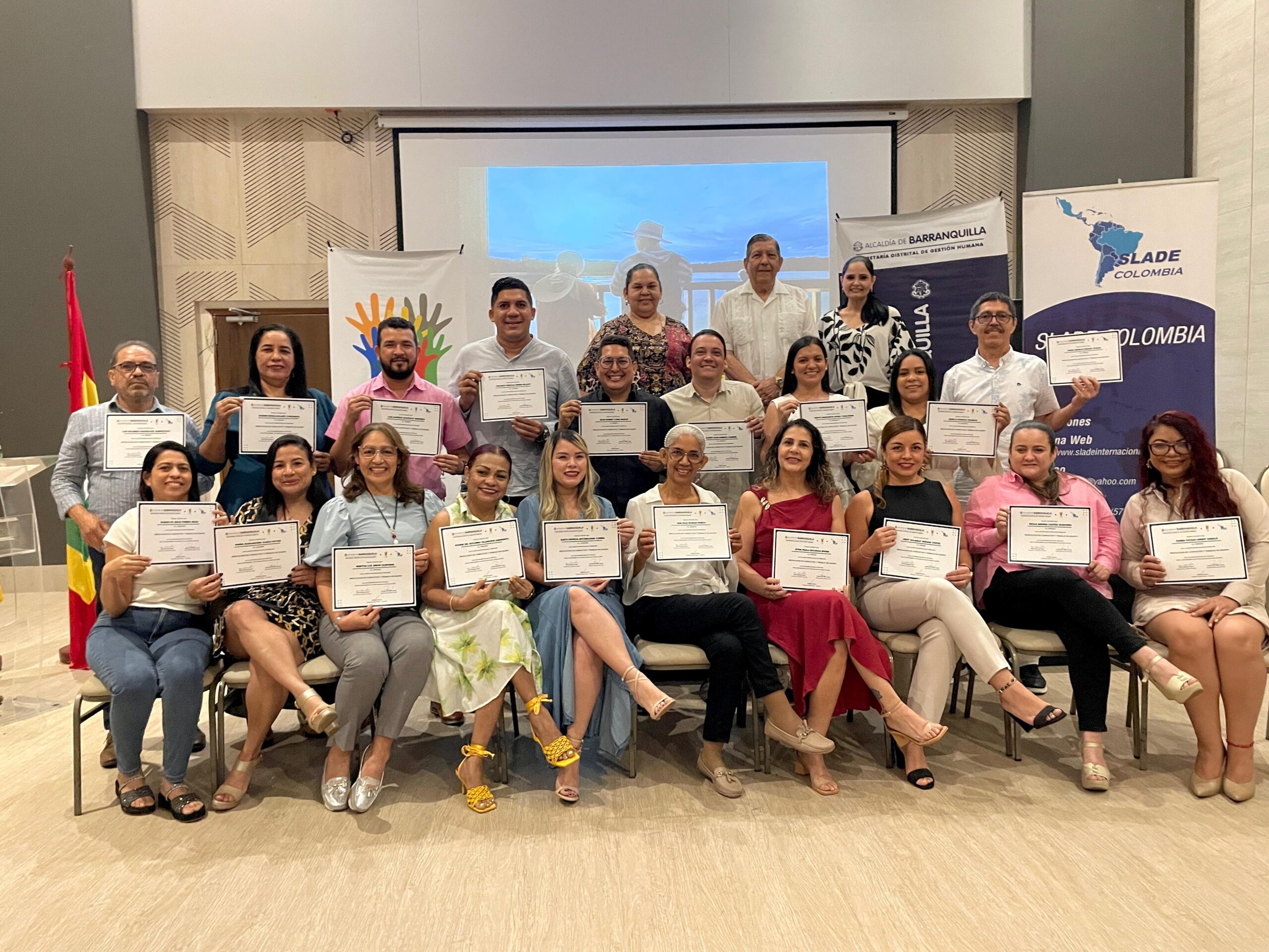Grupo de funcionarios en plano general, la primera fila sentados y los demás de pie, posando con su diploma.
