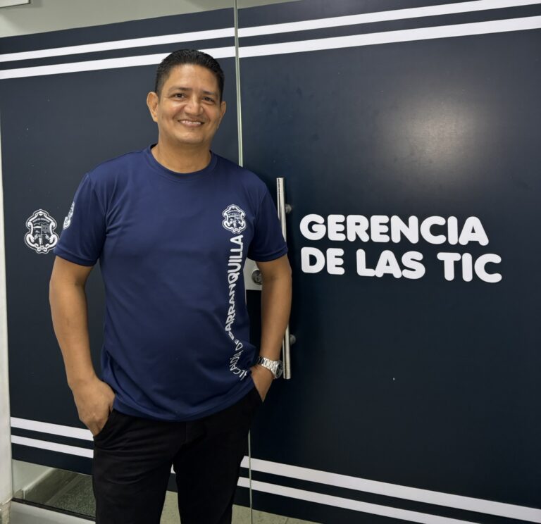 Funcionario de pie, en plano general, posando junto a la puerta de Gerencia TIC