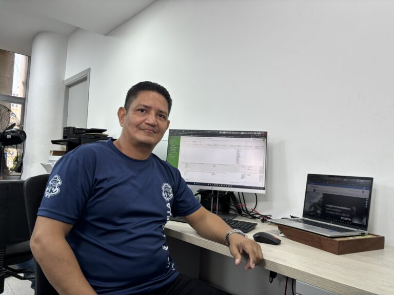 Funcinario en camiseta institucional, sentado junto a su escritorio.