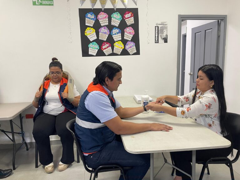 Funcionario sentado recibiendo masaje de mano,mientras una funcionaria al fondo de la imagen recibe masaje corporal.