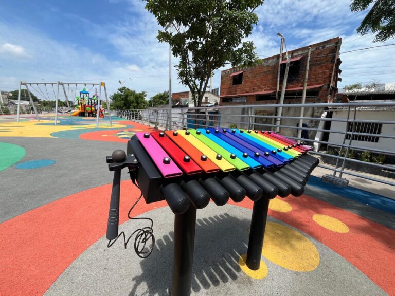Instrumento musical tipo xilófono gigante, diseñado para uso recreativo, con láminas en colores del arcoíris (rojo, naranja, amarillo, verde, azul y morado)