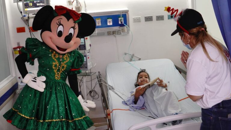 una niña sonriendo en habitación hospitalaria junto con minnie mouse y la directora de primera infancia 