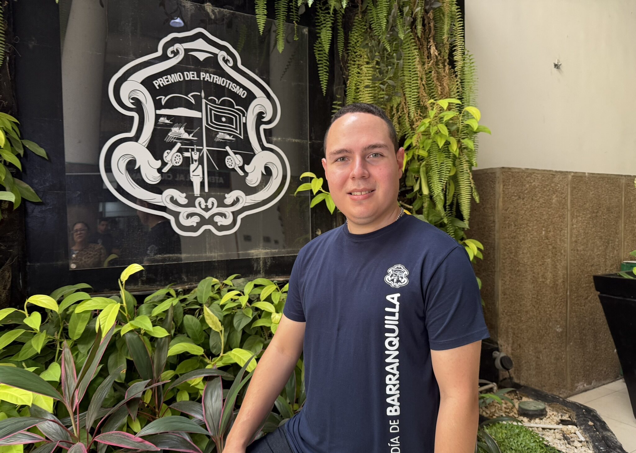 Funcionario con camiseta institucional, con fondo con el logo.