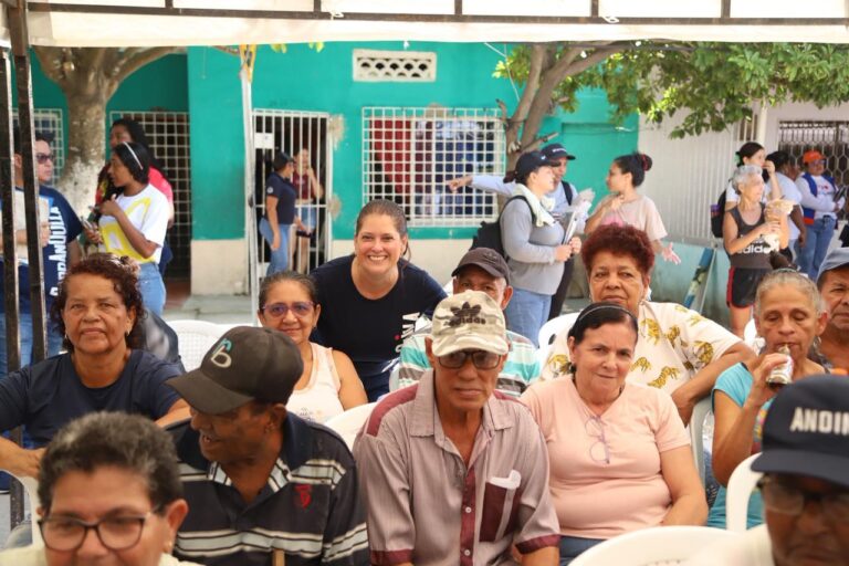 la gerente de Desarrollo Social compartiendo con un grupo de adultos mayores durante una jornada comunitaria. Ella se ubica detrás de ellos, sonriendo y mostrando cercanía, mientras los asistentes conversan y disfrutan del espacio.