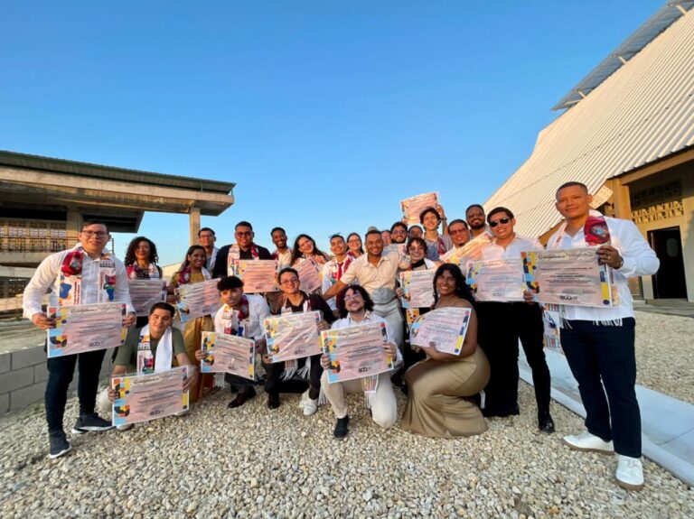 jóvenes recién certificados por la Escuela Distrital de Arte (EDA). Todos sostienen orgullosamente sus diplomas mientras posan al aire libre, bajo un cielo totalmente despejado.