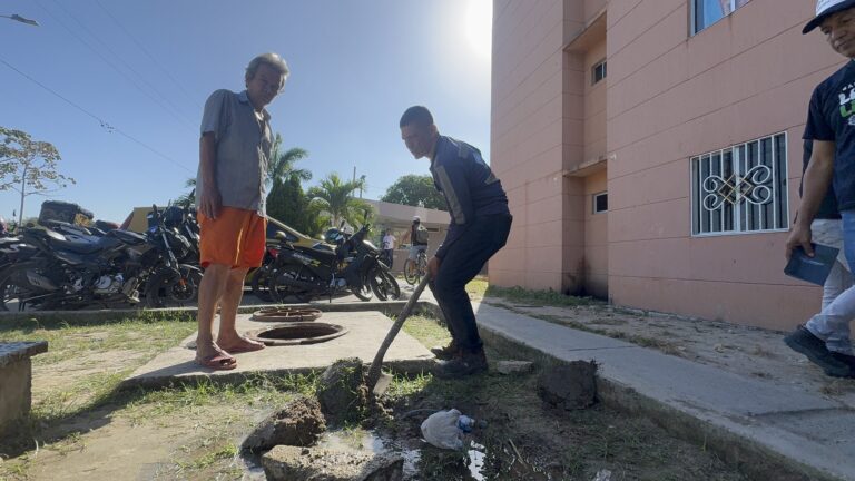 Persona utilizando una pala para cavar el suelo, donde se observa tierra removida y acumulación de agua, como parte de las labores de limpieza y mantenimiento de tuberías y alcantarillado.