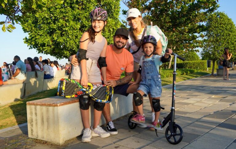 Grupo conformado por cuatro personas: dos niñas y dos adultos. Las niñas llevan rodilleras, coderas y cascos; la mayor está sobre patines y la menor en una scooter. Todas se muestran sonrientes, reflejando un ambiente de alegría y recreación.