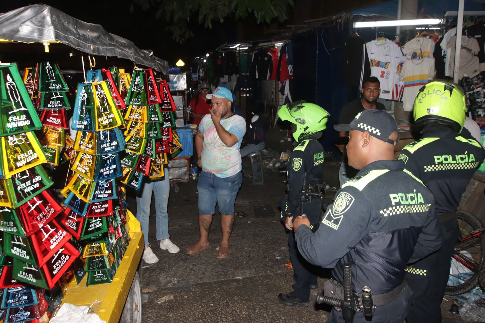 Varios policías inspeccionan un puesto callejero que exhibe faroles coloridos con mensajes navideños.