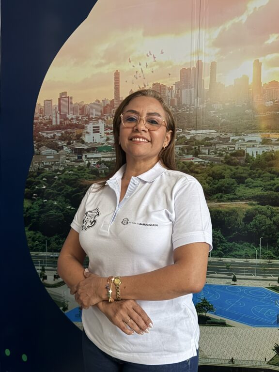 Funcionaria de pie, en plano medio, posando con brandind de Alcaldía detrás de ella.