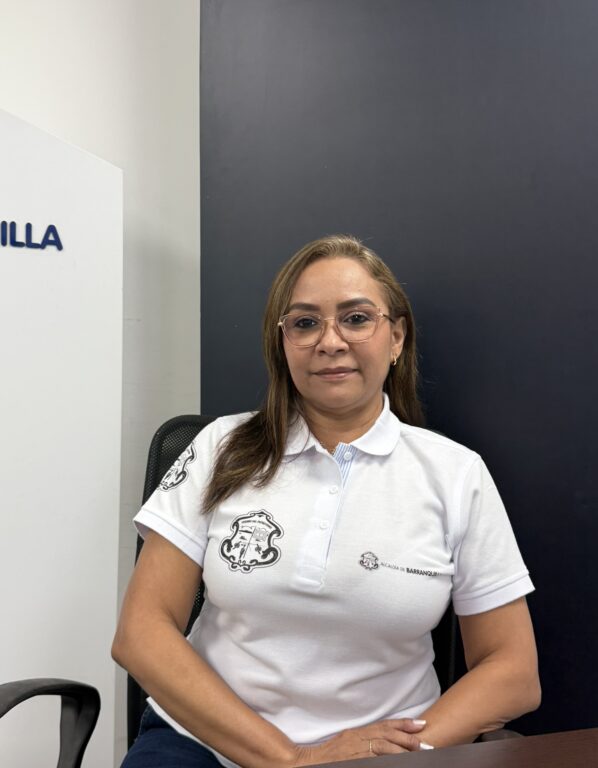 Funcionaria con camiseta institucional blanco, sentada en plano medio abierto.