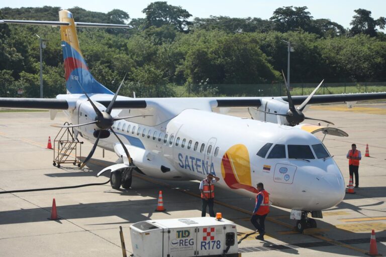 un avión ATR-72 de la aerolínea SATENA estacionado en una plataforma aeroportuaria. El avión es de color blanco con detalles en azul y amarillo, y lleva el logotipo de SATENA en el fuselaje.