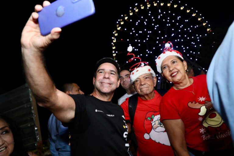 El acalde Alejandro Char, tomándose una selfie en un ambiente nocturno festivo, además llevan gorros navideños decorados con espirales rojas y detalles blancos.