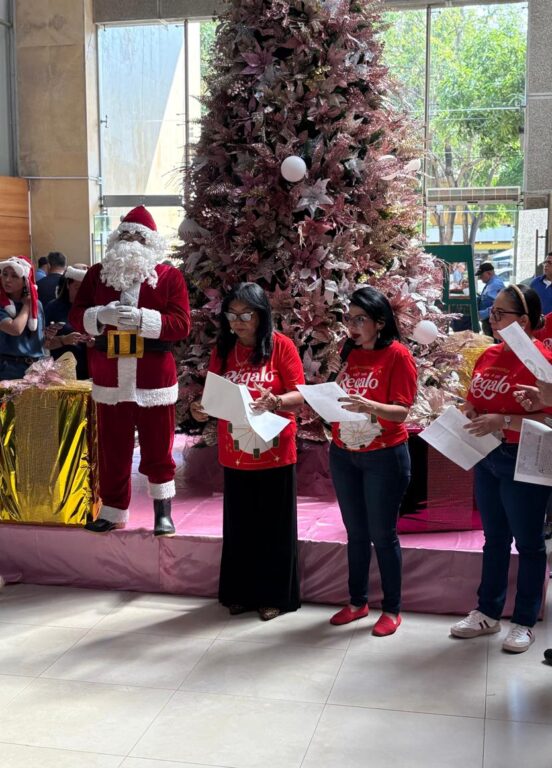 Funcionarios leyendo la novena, junto a arbol de Navidad y Santa.