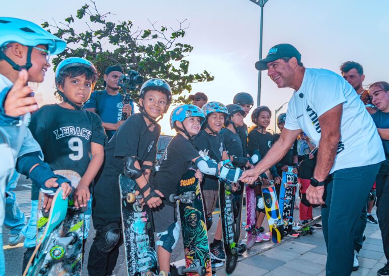 El Acalde Alejandro Char saludando a niños Todos llevan cascos protectores y equipo de seguridad, y sostienen patinetas de diferentes diseños y colores